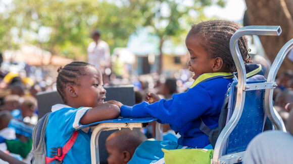 A girl in a wheelchair and her classmate talking together under a tree — inclusive education means every child belongs